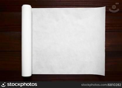 Roll of white baking paper photographed overhead on dark wood with natural light