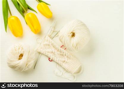 roll of white soft knitting yarn, knitting mittens and yellow tulips on lighten background