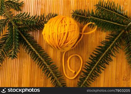 roll of yellow soft knitting yarn and yew branch on wooden background