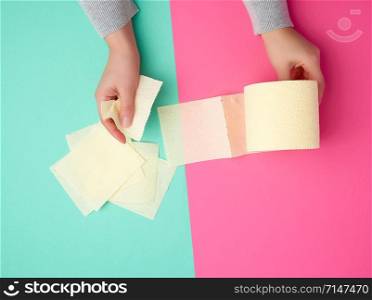 roll of yellow toilet paper in female hands, torn pieces on a colored background, top view
