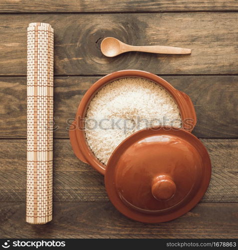 rolled up place mat with rice brown pot with lid wooden spoon