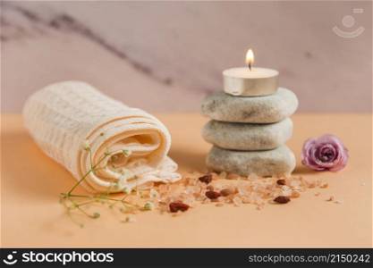 rolled up towel lighted candle spa stones rose himalayan salts peach colored backdrop