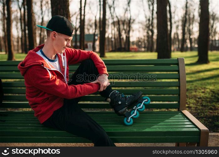 Roller skater posing on the bench in skates, city park on background. Male rollerskater leisure in city park