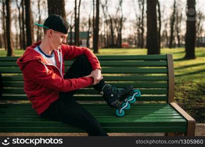 Roller skater posing on the bench in skates, city park on background. Male rollerskater leisure in city park