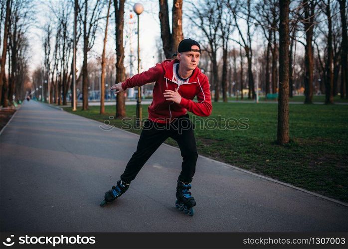 Roller skater rides by sidewalk in city park. Male rollerskater leisure