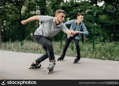 Roller skating, two male skaters begins speed race in summer park. Urban roller-skating, active extreme sport outdoors, rollerskating