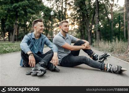 Roller skating, two male skaters sitting on the ground in park. Urban roller-skating, active extreme sport outdoors, rollerskating