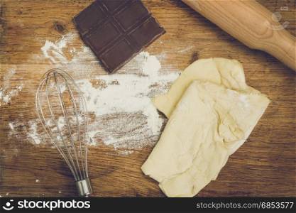 Rolling pin, chocolate, flour and dough lying on wooden board