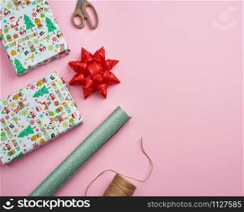 rolls with wrapping paper, brown rope, scissors, decor and a wrapped square box with a gift. DIY gift making process, pink background