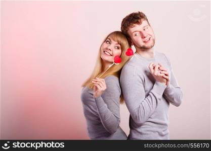 Romance love relationship valentines concept. Cheerful couple fooling together. Young man with woman holding hearts on sticks.. Cheerful couple fooling together.