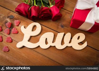 romance, valentines day and holidays concept - close up of word love, gift box, red roses and heart-shaped candies on wood