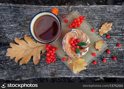 Romantic autumn still life with basket cake, cup of tea, rowan berries and leaves at wooden board, top view. Romantic autumn still life