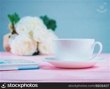 Romantic background with cup of tea or coffee, rose flowers and book over light pink wooden table