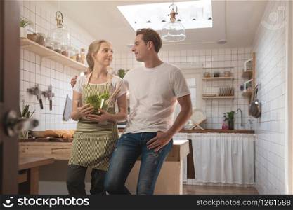 Romantic caucasian couple in love having great time together in the kitchen.Happy young man and woman in kitchen hand hold blow of salad and look at each other with smiling face.
