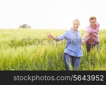 Romantic Couple Running In Field Holding Hands