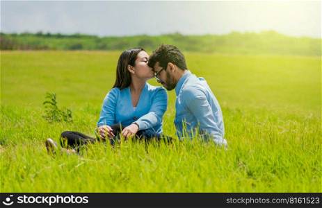 Romantic couple sitting on the grass kissing their foreheads, A pretty girl kissing her boyfriend&rsquo;s forehead in the field, A couple in love sitting on the field kissing their foreheads