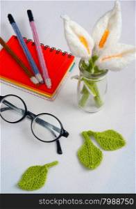 Romantic desk with ornament from handmade product, lily flower knit from white yarn, handbook, knitting pencil, coffee cup, glasses, beautiful craft