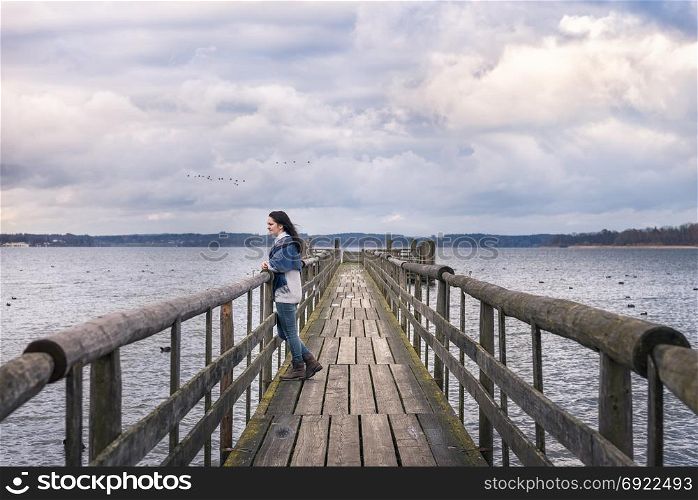 Romantic destination theme image with a woman, sitting alone on a rustic bridge, over the famous Chiemsee lake, at sunset, enjoying the peacefulness of nature.