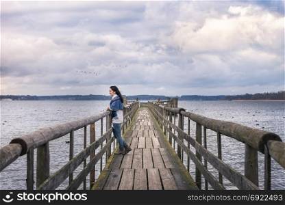 Romantic destination theme image with a woman, sitting alone on a rustic bridge, over the famous Chiemsee lake, at sunset, enjoying the peacefulness of nature.