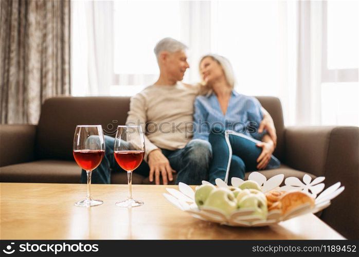 Romantic dinner of adult love couple at home. Mature husband and wife sitting on couch and embrancing, happy family. Romantic dinner of adult love couple at home
