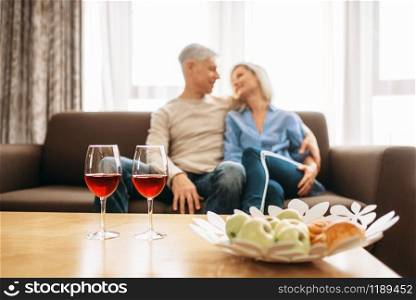 Romantic dinner of adult love couple at home. Mature husband and wife sitting on couch and embrancing, happy family. Romantic dinner of adult love couple at home