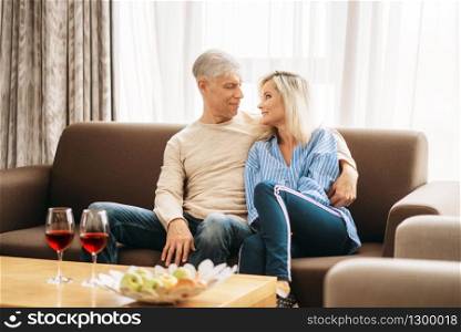 Romantic dinner of adult love couple at home. Mature husband and wife sitting on couch and embrancing, happy mature family. Romantic dinner of adult love couple at home