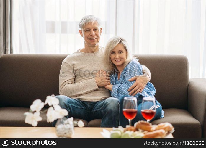 Romantic dinner of adult love couple at home. Mature husband and wife sitting on couch and embrancing, happy family