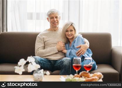 Romantic dinner of adult love couple at home. Mature husband and wife sitting on couch and embrancing, happy family