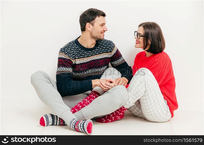 Romantic female and male hold hands together, look at each other with love, have good relationship, wears knitted sweaters, have positive expressions, isolated on white background. Relationship