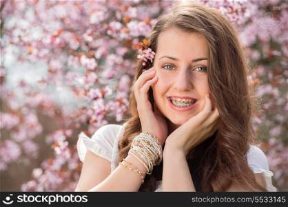 Romantic girl with braces touching cheek near blossoming tree spring