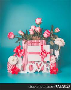Romantic greeting setting with word LOVE, gift box, heart, bunch of pink pale roses , white bottle of champagne and glasses on turquoise blue background, front view. Modern layout or mock up for card
