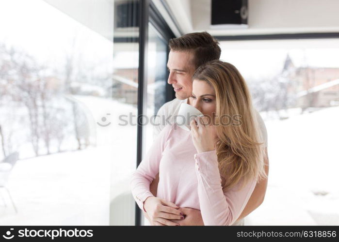 romantic happy young couple enjoying morning coffee by the window on cold winter day at home