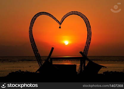 Romantic heart shaped silhouette with chairs on a scenic tropical beach at sunset