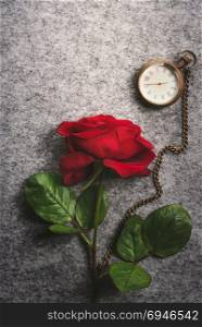 Romantic image with a beautiful single red rose and an antique pocket clock, on a retro fabric background.