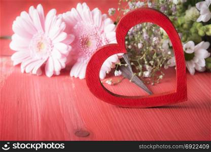 Romantic image with a bright red wooden heart and a bouquet of lovely flowers, on a wooden table. A concept of love, valentine day or greeting card.
