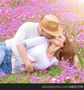 Romantic kisses outdoors, attractive man kissing his beautiful young wife lying down on pink floral meadow, spring time concept