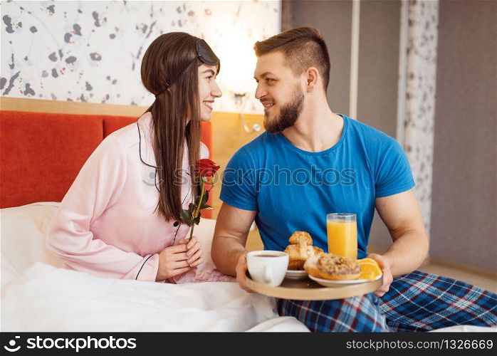 Romantic love couple, breakfast and flowers in bed at home, good morning. Harmonious relationship in young family. Man and woman resting together in their house, carefree weekend. Romantic love couple, breakfast and flowers in bed