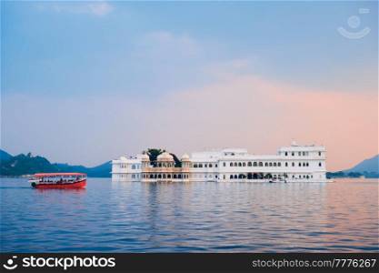 Romantic luxury India travel tourism - tourist boat in front of Lake Palace (Jag Niwas) complex on Lake Pichola on sunset with dramatic sky, Udaipur, Rajasthan, India. Lake Palace palace on Lake Pichola in twilight, Udaipur, Rajasthan, India