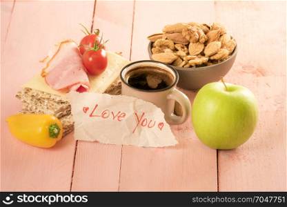 Romantic message wrote on a piece of paper near a cup of coffee and delicious breakfast, on a pink wooden table
