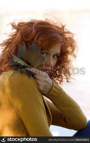 romantic portrait of a young woman with her face behind autumn leaves