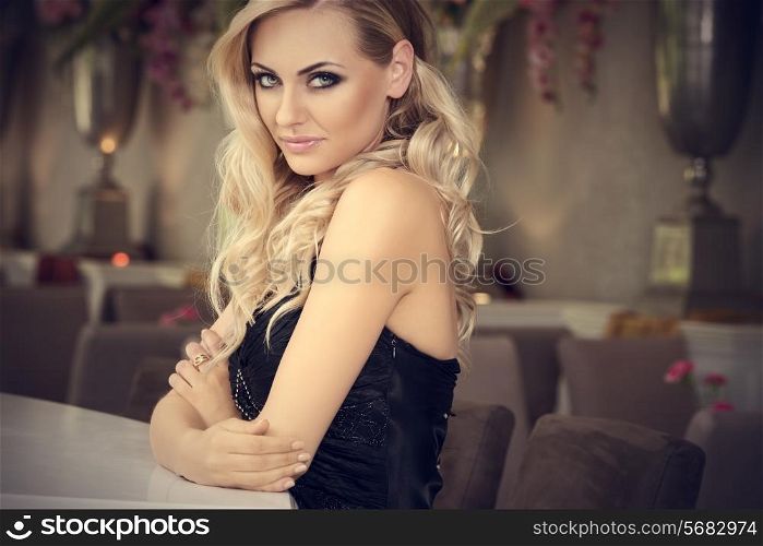 romantic portrait of cute beautiful blond with curly hair in luxury bar . loooking in camera smiling