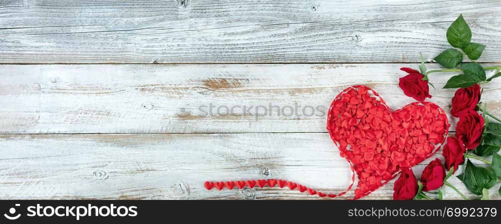 Romantic red roses and filled heart shaped ribbon on white rustic wooden background
