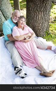 Romantic senior couple relaxes together outdoors under the trees.