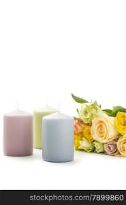Romantic still life with roses and candles. Romantic still life with a bunch of colorful fresh roses in pretty pastel shades and a trio of unlit candles in matching colors over white with copyspace for a Valentines or anniversary greeting