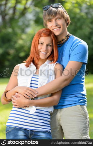 Romantic teenage couple hugging in sunny park smiling at camera