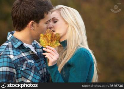 Romantic Teenage Couple Kissing Behind Autumn Leaf