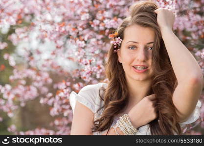 Romantic teenage girl wearing braces posing near blossoming tree spring