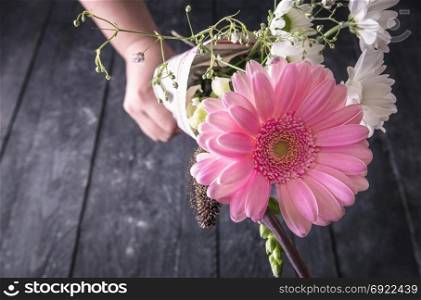 Romantic theme image with a lovely bouquet of Chrysanthemum flowers, wrapped in newspaper, held in hand and point it to the camera, on a vintage wooden background.
