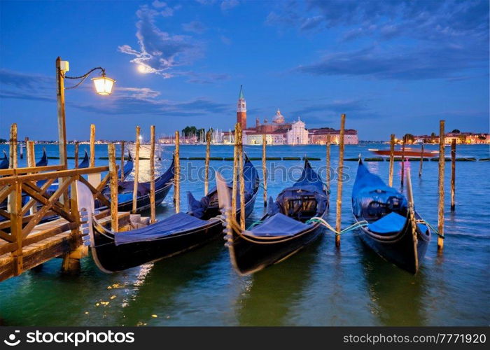 Romantic vacation Venice travel background - gondolas at Saint Mark  San Marco  square and Basilica San Giorgio Maggiore Church seen across Venice lagoon with full moon. Venice, Italy. San Giorgio Maggiore Church with full moon. Venice, Italy