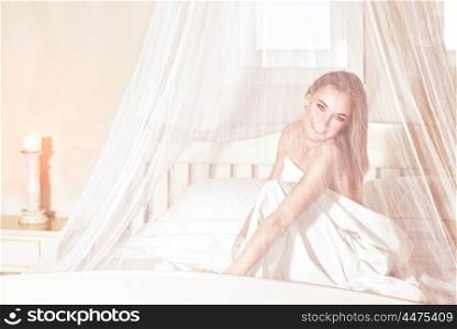Romantic woman sitting in the bed under gentle transparent valance, spending weekend in luxury spa hotel, enjoying rest and relaxation